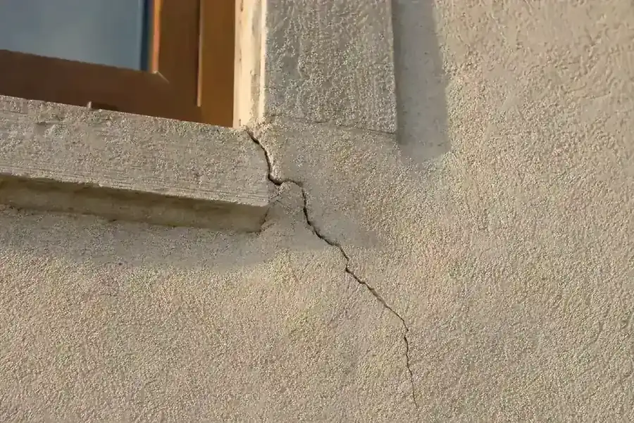 Fissure oblique sur le crépi d'une maison, partant de l'angle d'une fenêtre