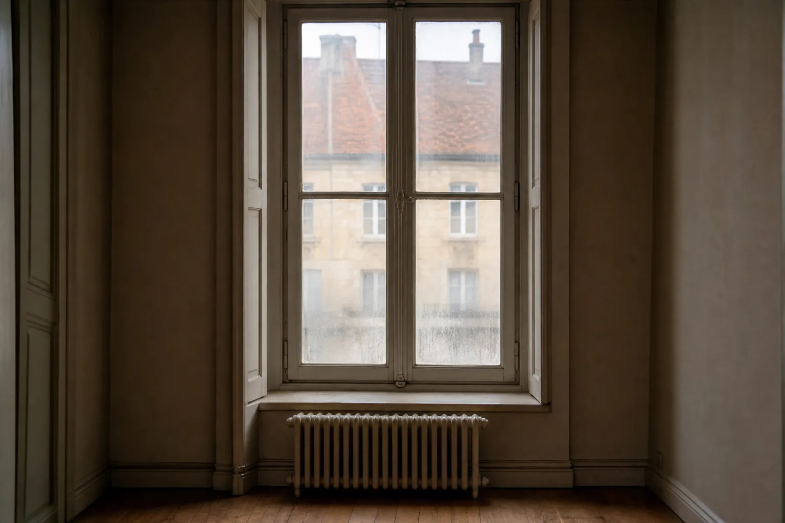 Fenêtre ancienne à simple vitrage et radiateur en fonte dans un logement vide